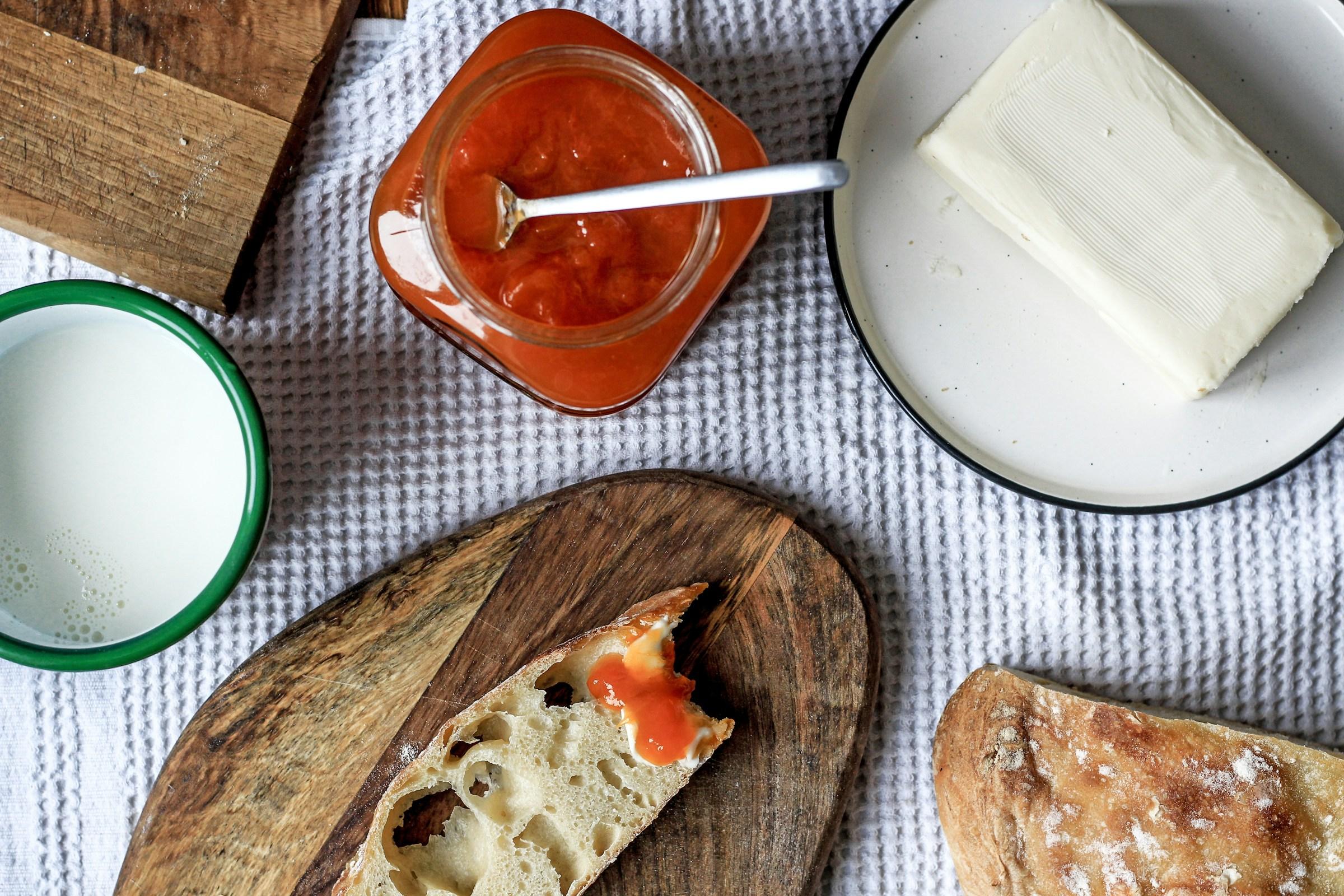 Keten örtü üzerinde reçel kavanozu, tereyağı, süt ve taze ekmek